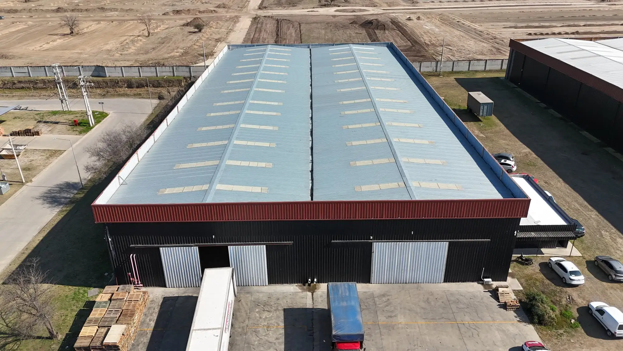 Nave industrial terminada de cerramiento negro con banda bordó, con dos portones y un camión cargando