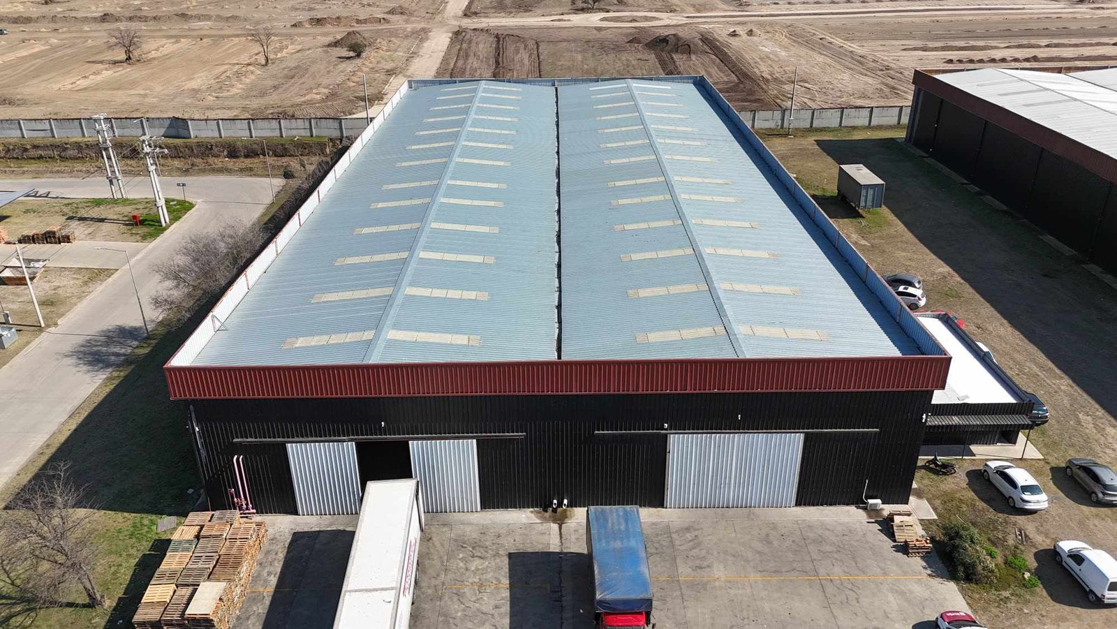 Nave industrial terminada de cerramiento negro con banda bordó, con dos portones y un camión cargando