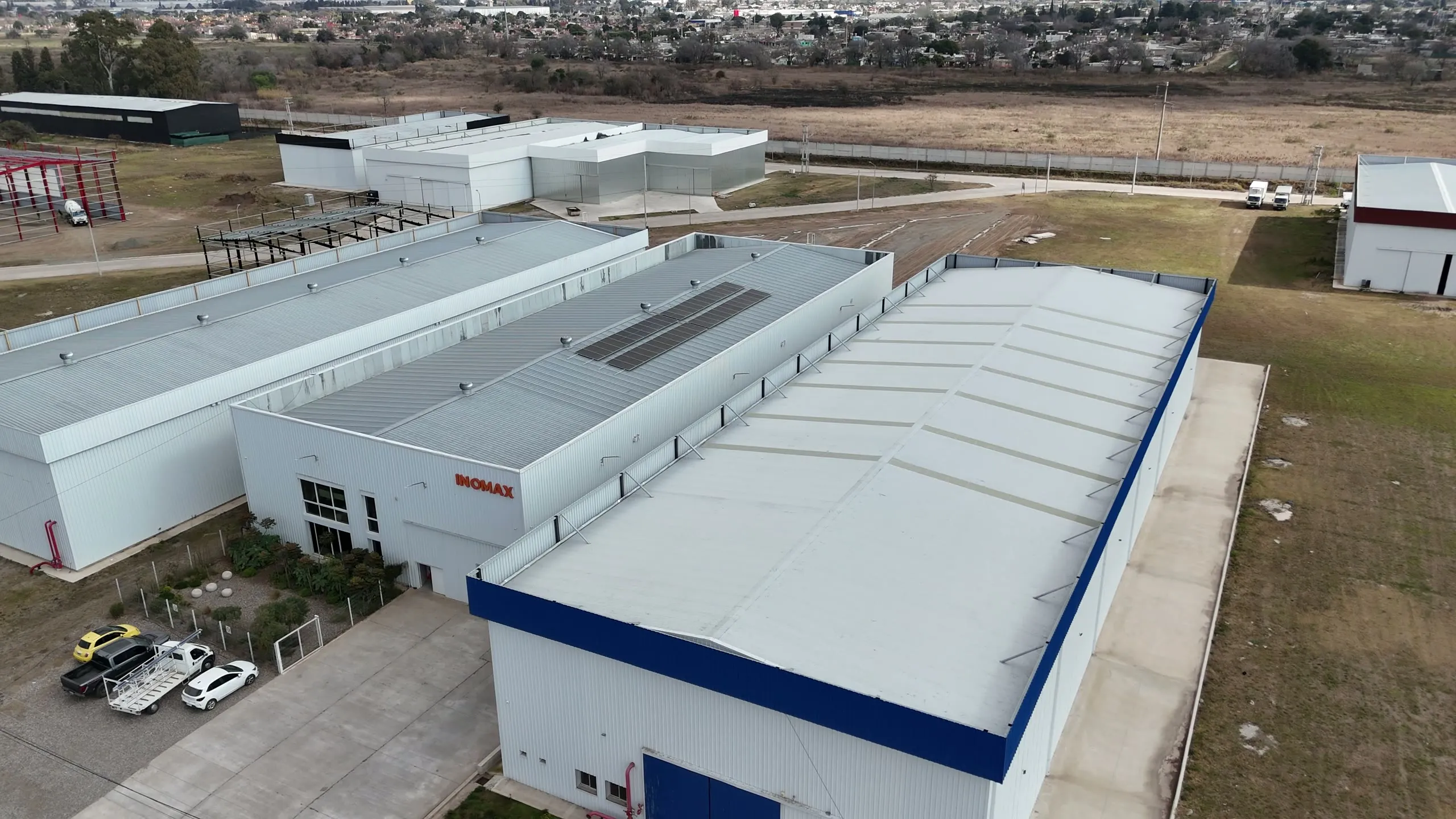 Vista aérea de una nave de techo curvo terminada junto a la planta industrial del cliente