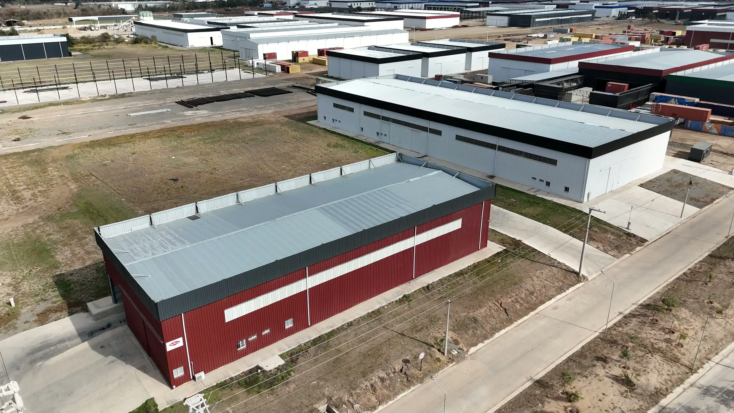 Vista aérea de una nave industrial terminada de muros bordó, al borde de un parque industrial