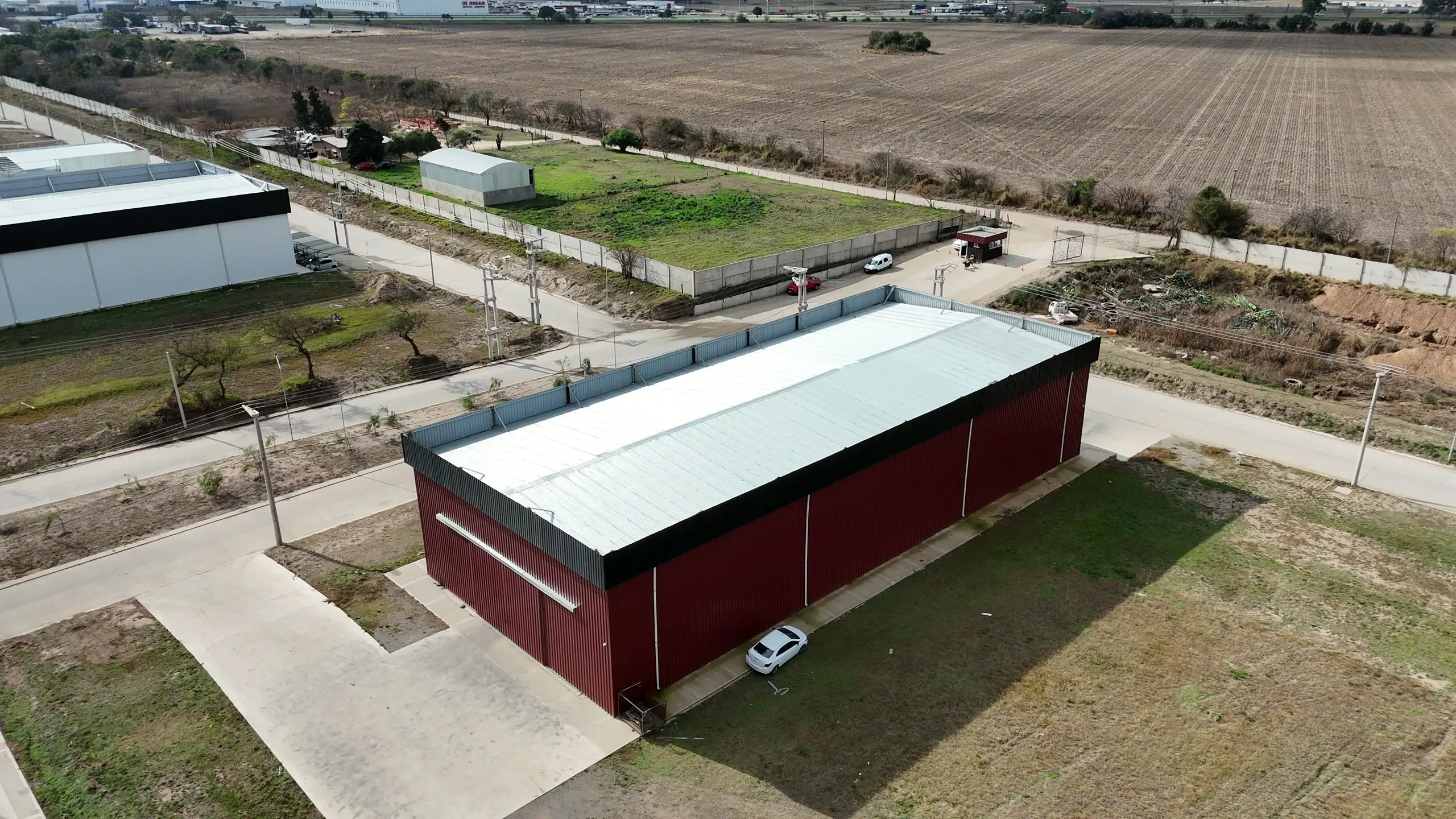 Vista aérea de una nave industrial de muros bordó con franja de chapa traslúcida lateral