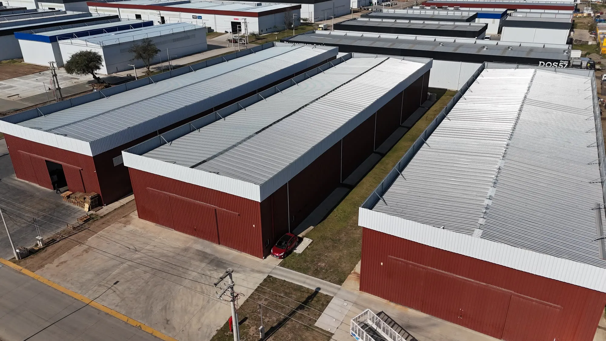 Naves industriales terminadas en fila, con cerramiento oscuro y banda perimetral bordó