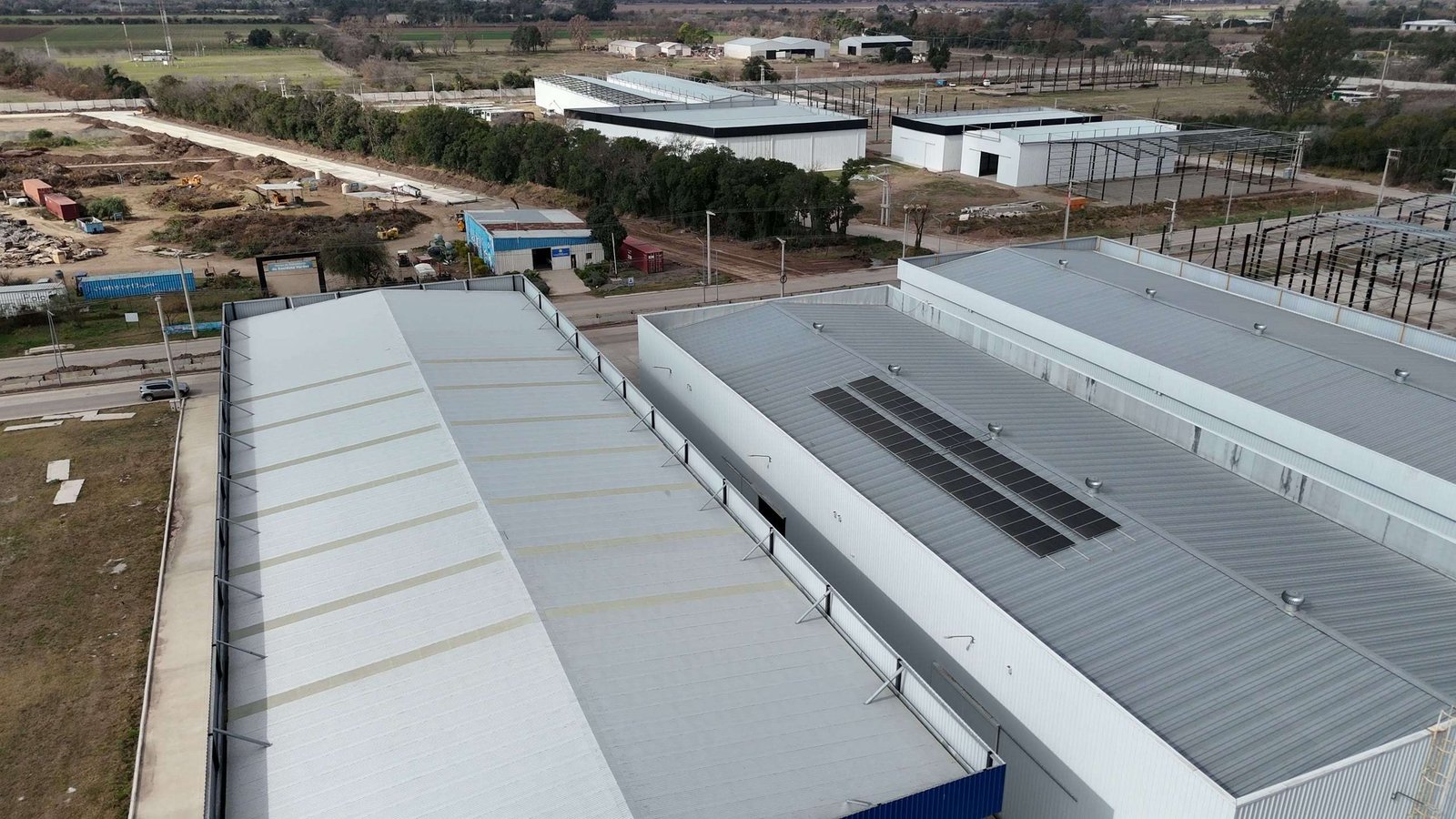 Vista aérea de una nave industrial de techo curvo terminada, junto a la planta del cliente